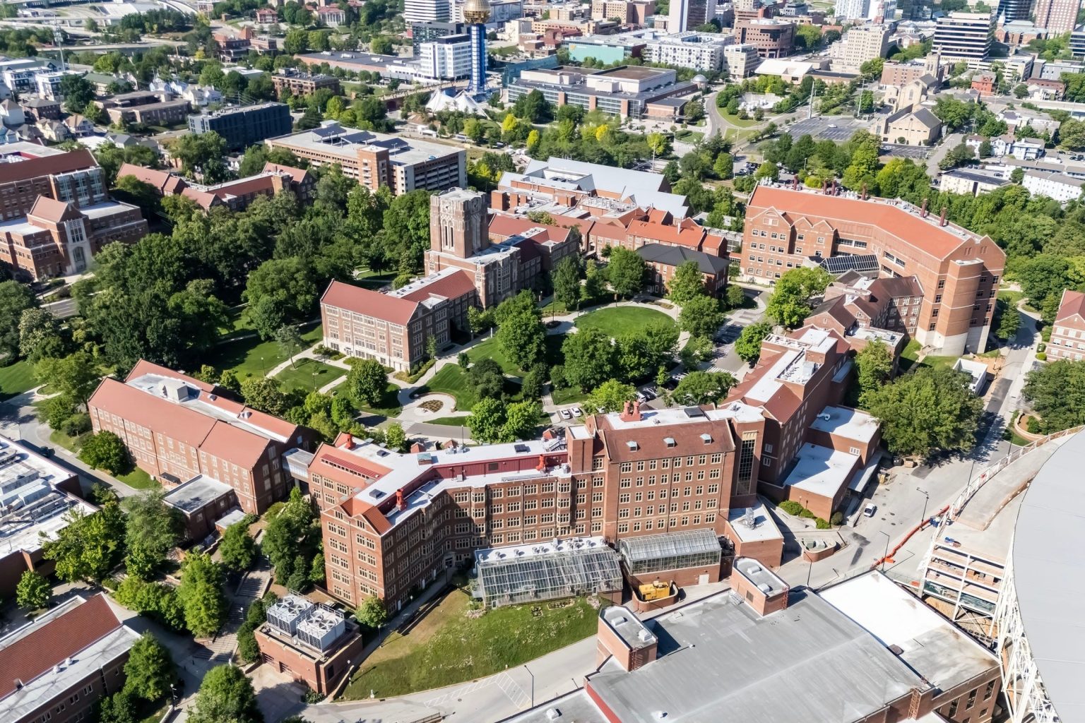 An aerial view of the University of Tennessee, Knoxville showcases a sprawling campus with lush greenery, historic buildings, modern research facilities.