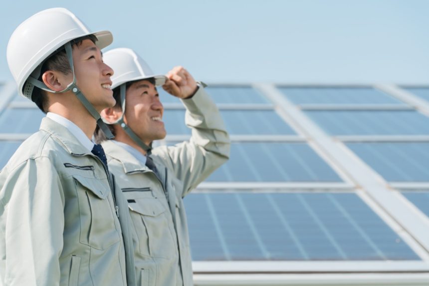 Photovoltaic power generation - Electrician and technician in work clothes standing in front of a solar panel (clean energy).