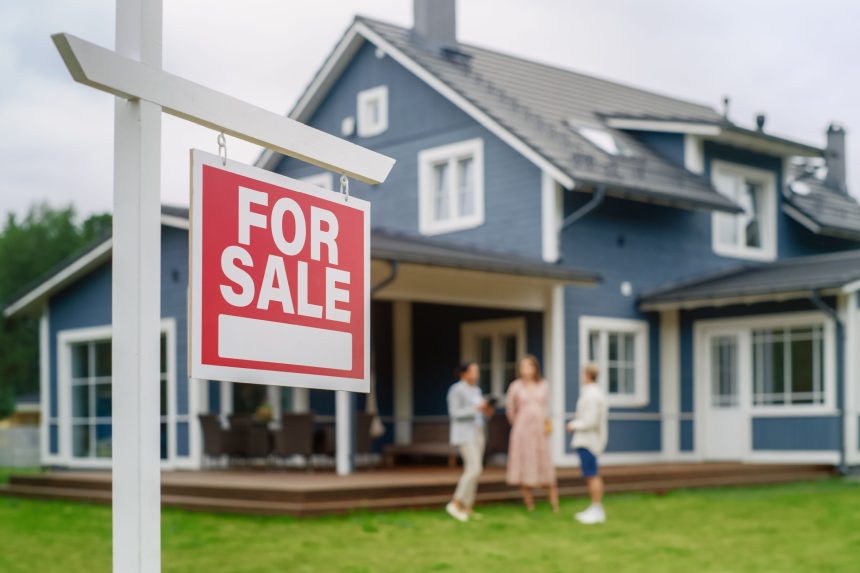 Young Couple Visiting a Potential New Home Property with Professional Real Estate Agent. Female Realtor Showing the Area to Future Homeowners. Focus on For Sale Sign.