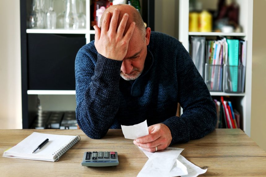 Man upset headache depressed from family cost got higher doing accounting holding receipts from supermarket with calculator by rising grocery prices and surging cost as an inflation financial crisis.
