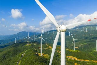 Aerial view of a wind farm with large wind turbines on green mountain for renewable energy production